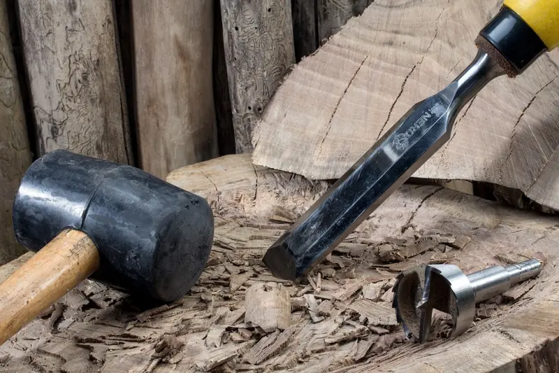 Wood chisel, mallet and drill bit on a block of timber