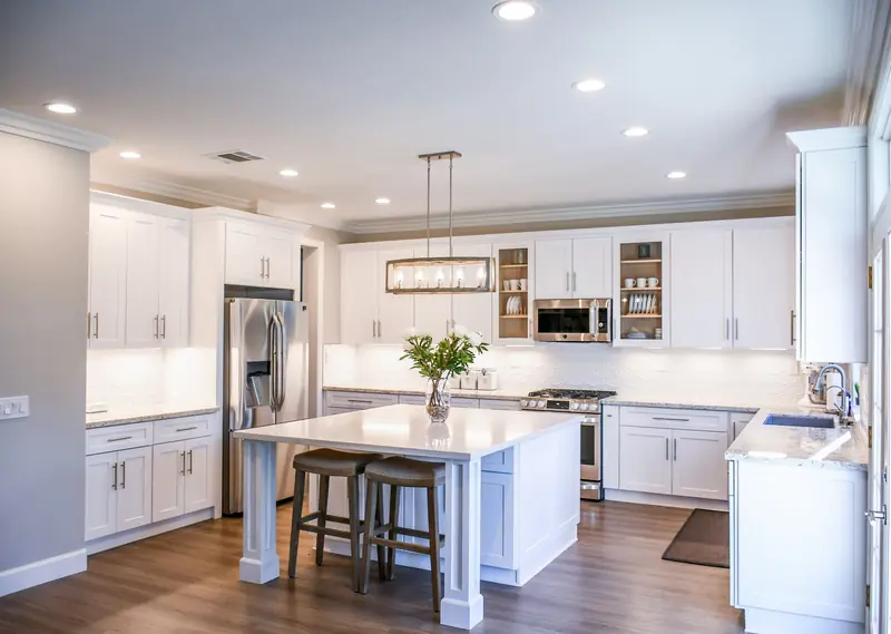 Bright fitted kitchen with white shaker cabinets, an island with stools and a wood floor